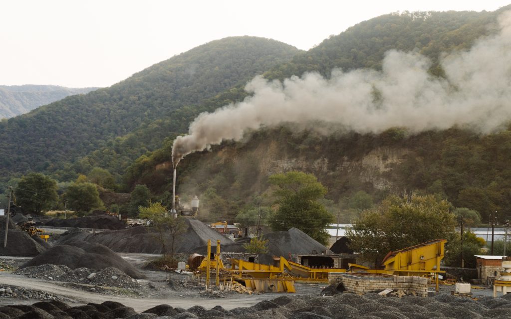 coal mining in the mountains, the mountains are covered with green trees, smoke is coming